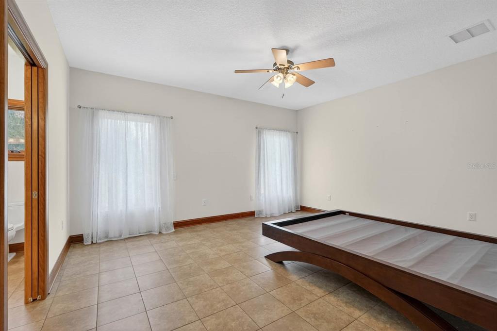 A bedroom with tile flooring, a ceiling fan, two windows with curtains, and a bed frame — 115 TANGELO TERRACE, CRESCENT CITY, FL