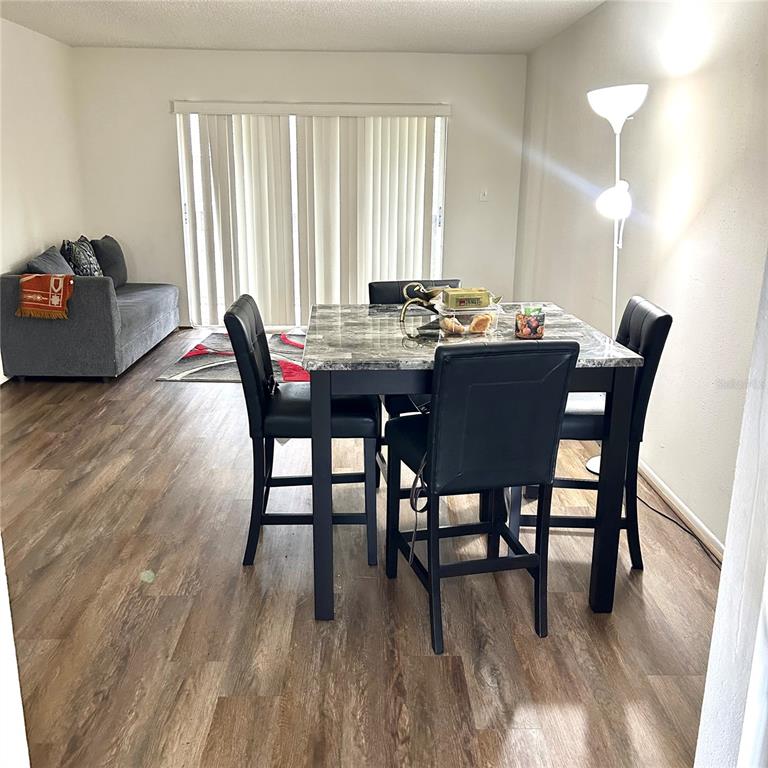 A dining area with a marble-topped table and black chairs sits before a living room — 7531 PITCH PINE CIRCLE UNIT 197, TAMPA, FL