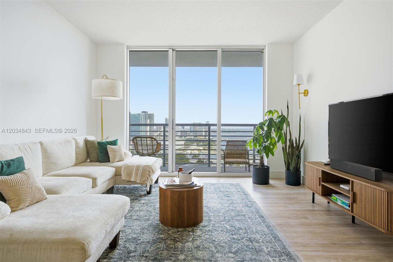 A living room features a white sectional sofa, a wooden coffee table, and a balcony view — 325 S Biscayne Blvd # 4022, Miami FL 33131, MIAMI, FL