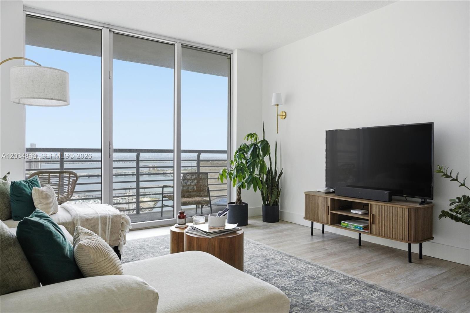 A living room features a television on a wooden console, a sofa, and balcony views — 325 S Biscayne Blvd # 4022, Miami FL 33131, MIAMI, FL