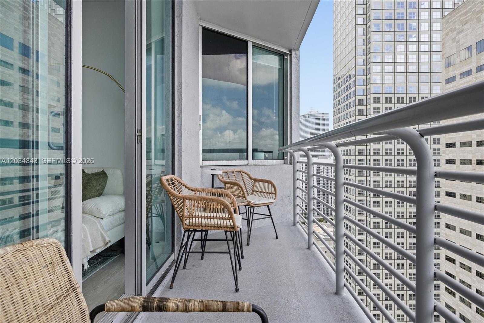 A balcony with three wicker chairs overlooks a city skyline with tall buildings — 325 S Biscayne Blvd # 4022, Miami FL 33131, MIAMI, FL