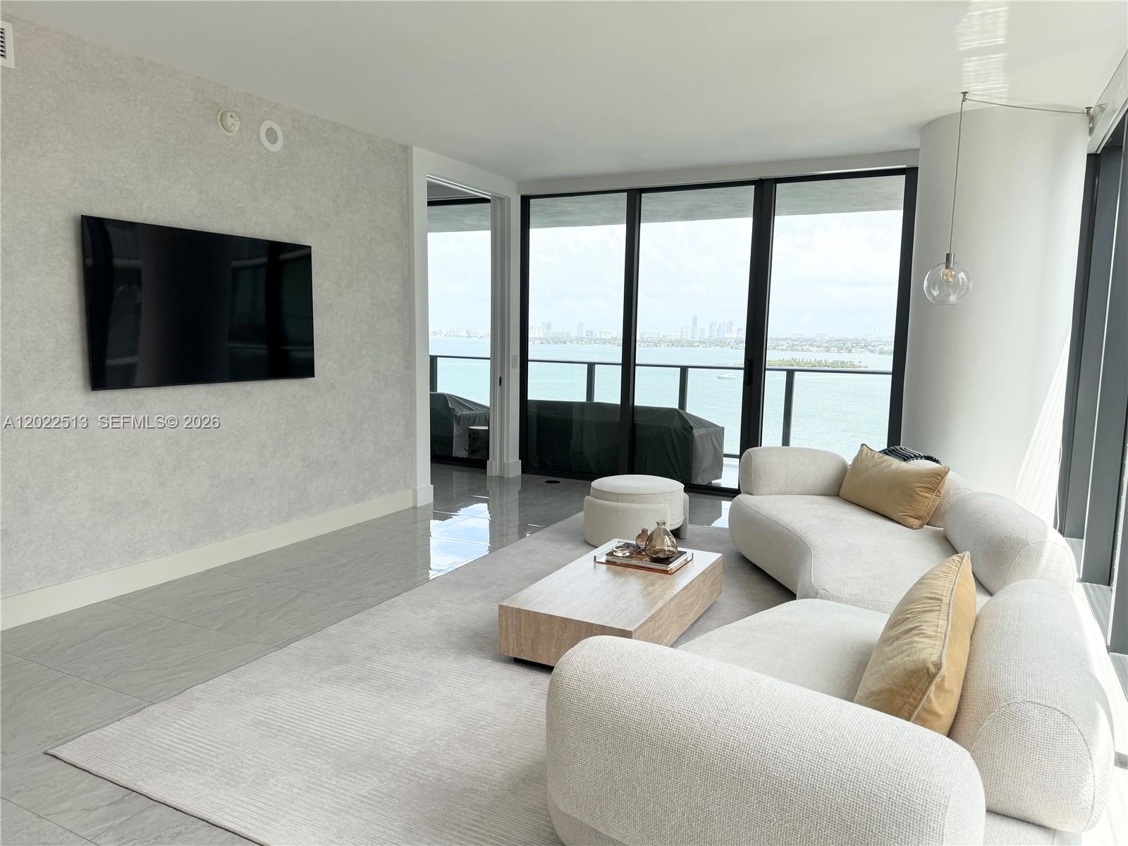 A living room features a curved sofa, a wooden coffee table, and floor-to-ceiling windows — 650 NE 32nd St # 1901, Miami FL 33137, MIAMI, FL