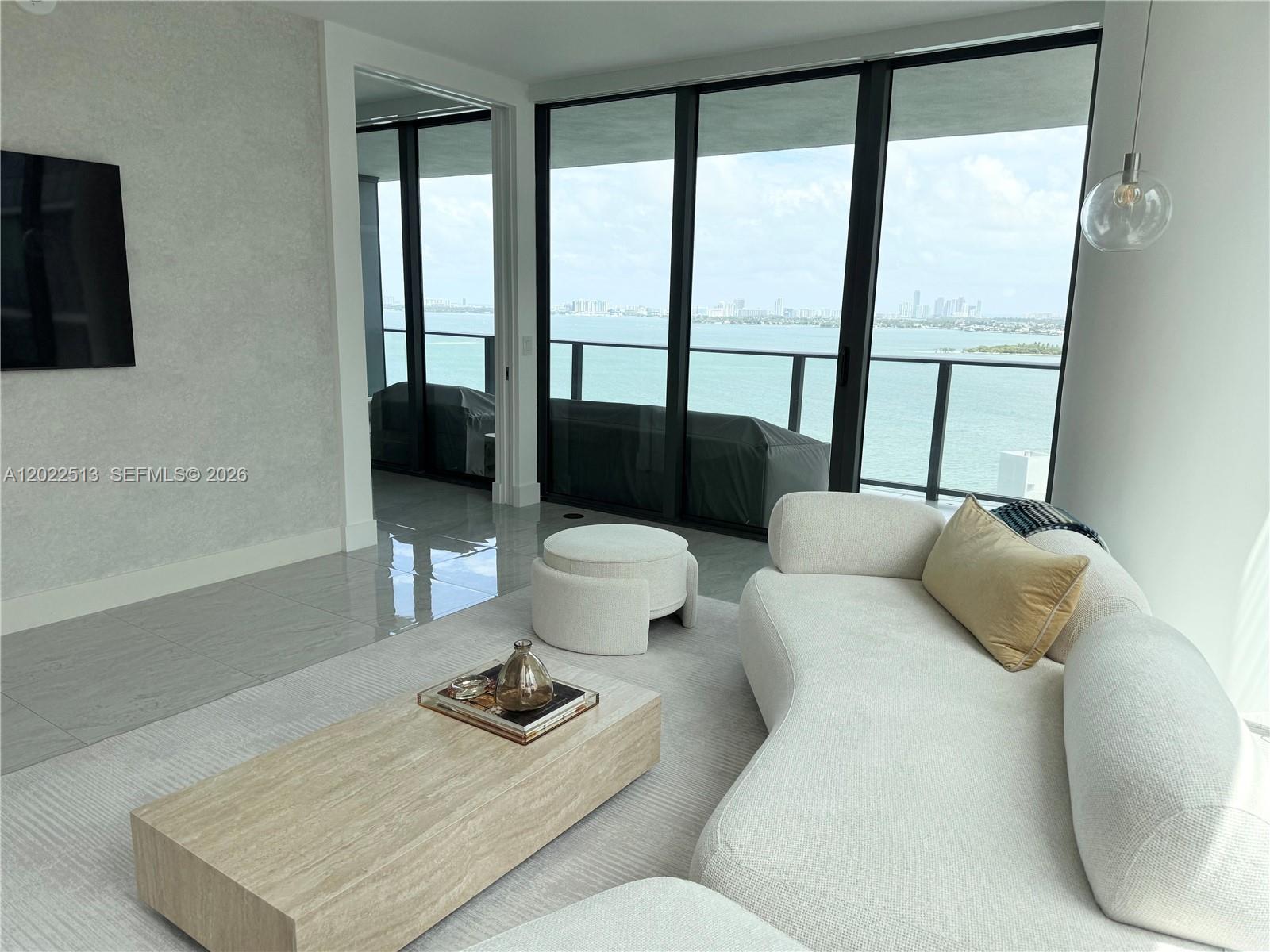 A modern living room features a curved white sofa, stone coffee table, and balcony views — 650 NE 32nd St # 1901, Miami FL 33137, MIAMI, FL