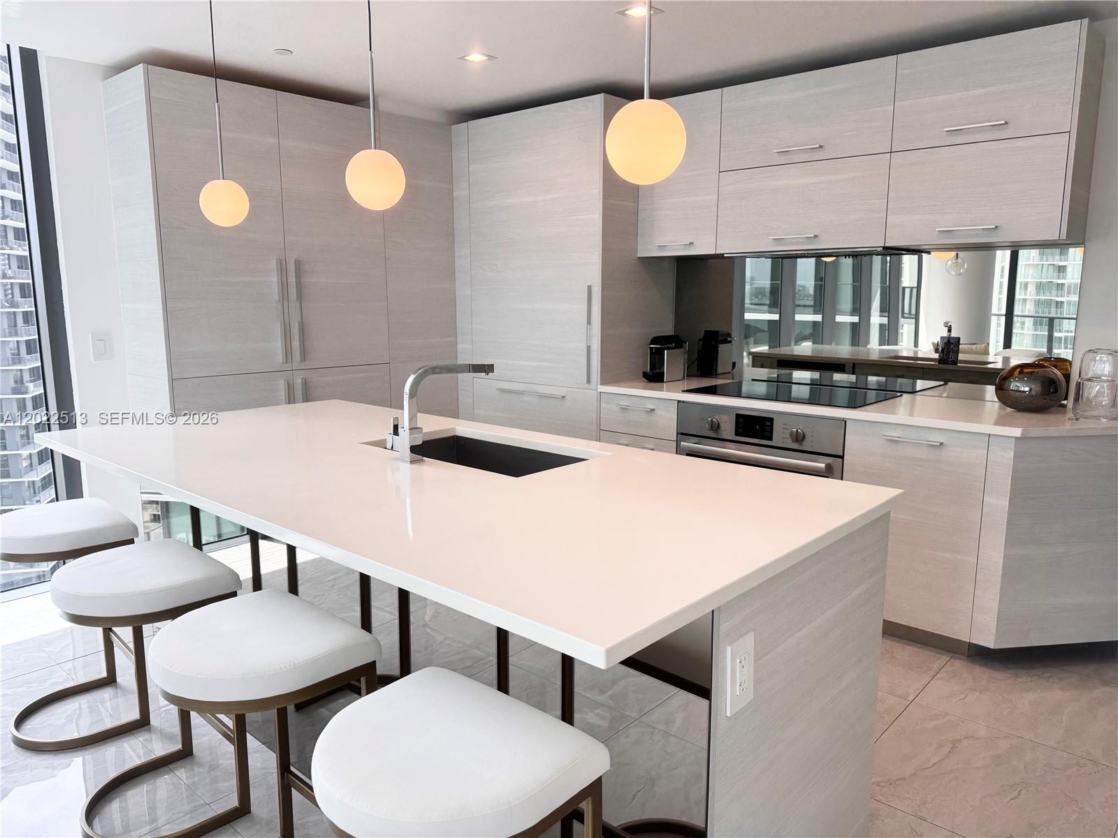 A modern kitchen features light wood cabinetry, a white island with a sink, and pendant lights — 650 NE 32nd St # 1901, Miami FL 33137, MIAMI, FL