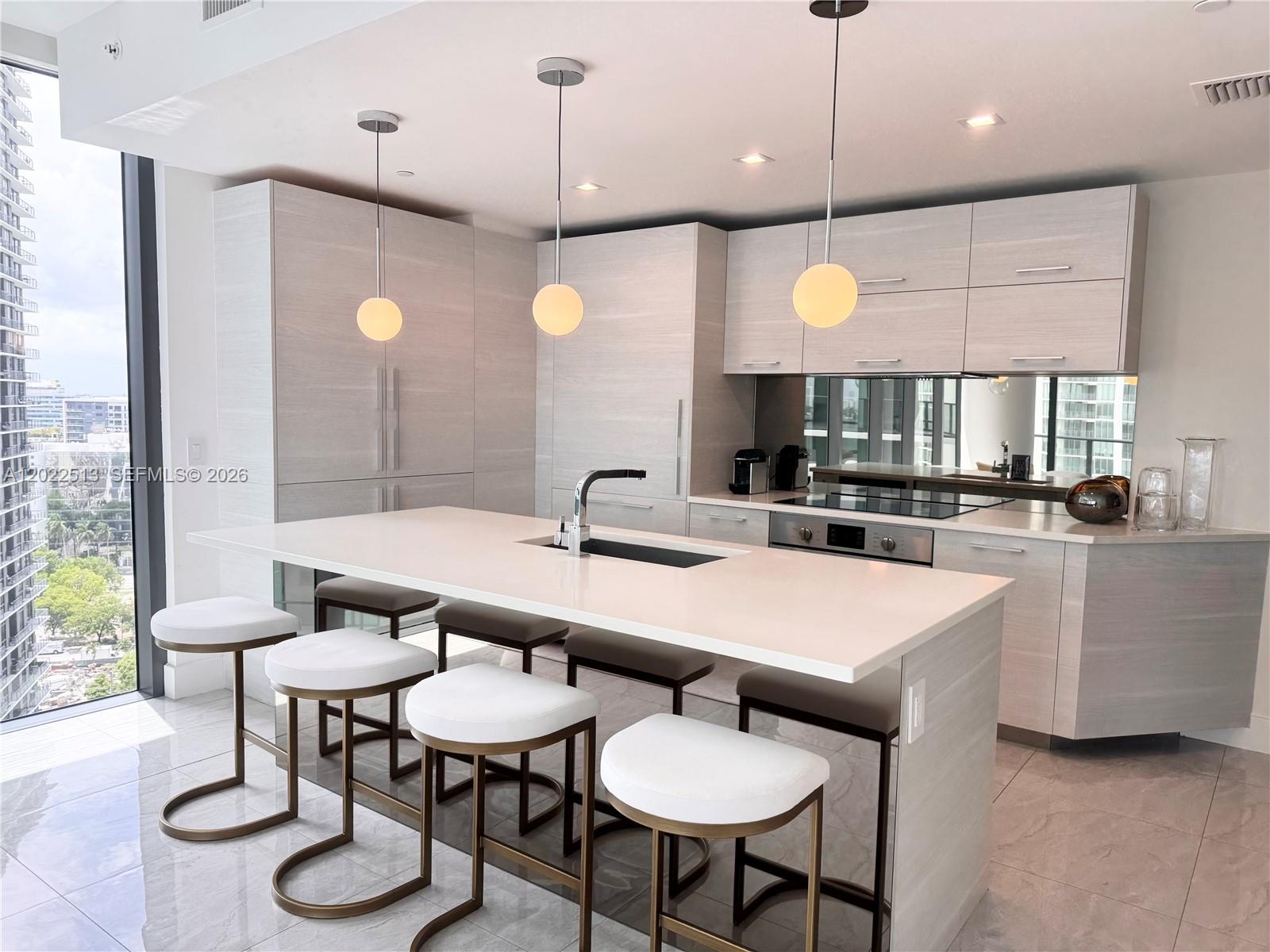 A modern kitchen features light wood cabinetry, a white island with bar stools, and floor-to-ceiling windows — 650 NE 32nd St # 1901, Miami FL 33137, MIAMI, FL