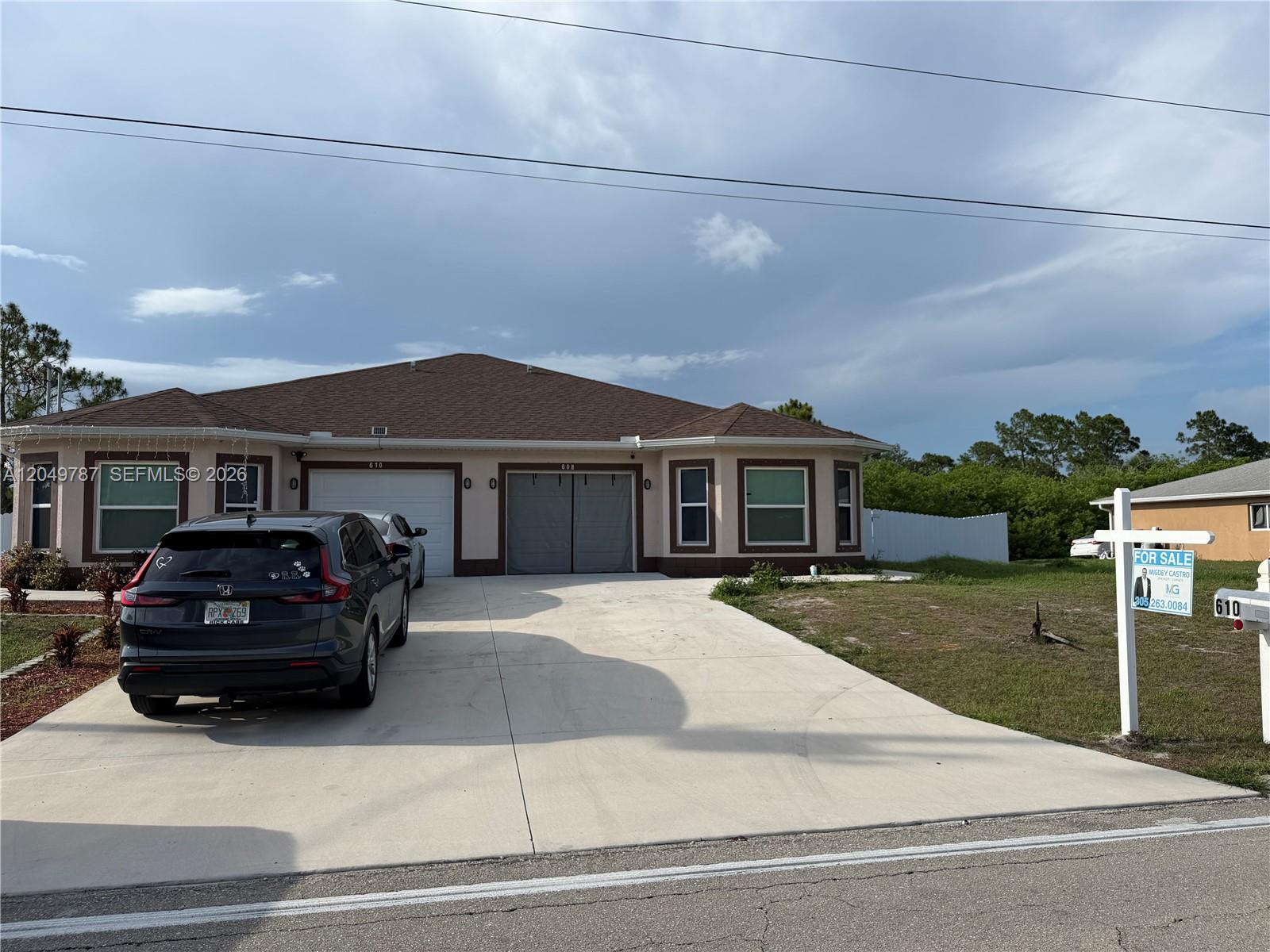 A single-story house with a two-car garage and a driveway under a cloudy sky — 610 W 12, Lehigh Acres FL 33972, LEHIGH ACRES, FL