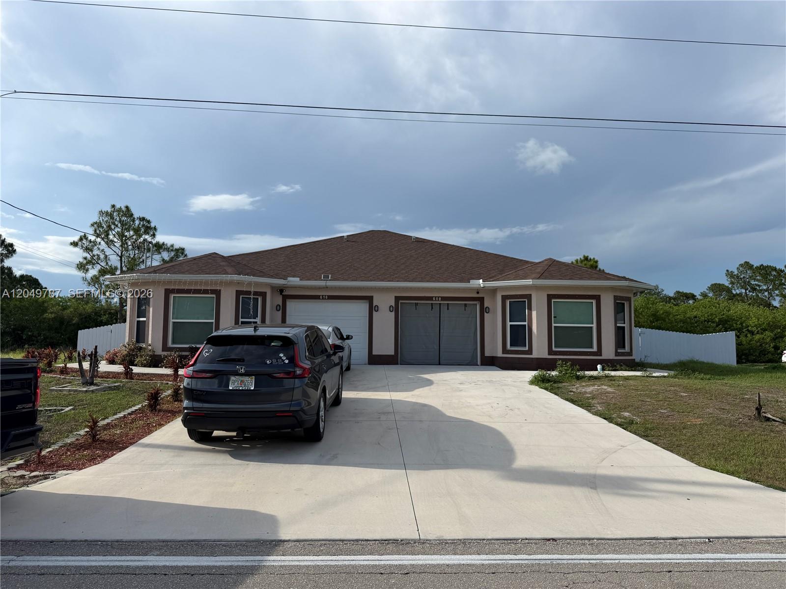 A single-story duplex with a concrete driveway, two garage doors, and a brown roof — 610 W 12, Lehigh Acres FL 33972, LEHIGH ACRES, FL
