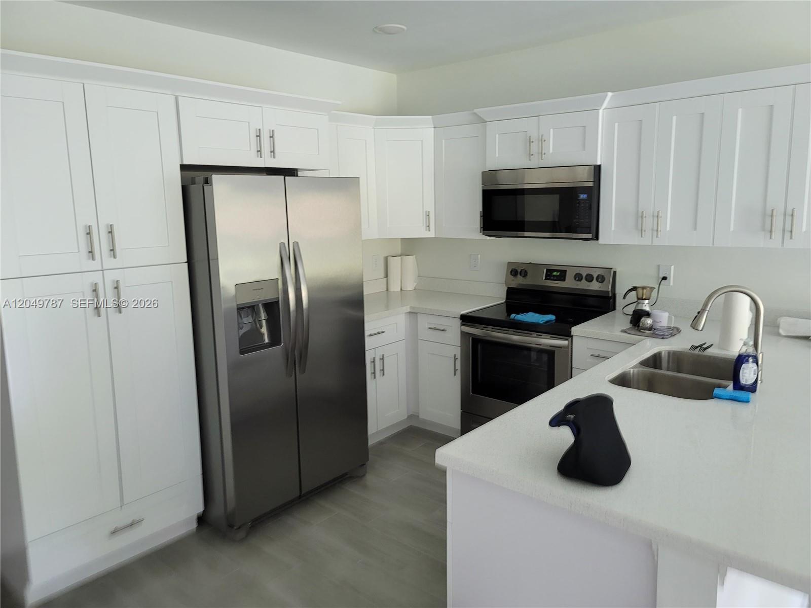 A modern kitchen features white cabinetry, stainless steel appliances, and a white quartz countertop — 610 W 12, Lehigh Acres FL 33972, LEHIGH ACRES, FL