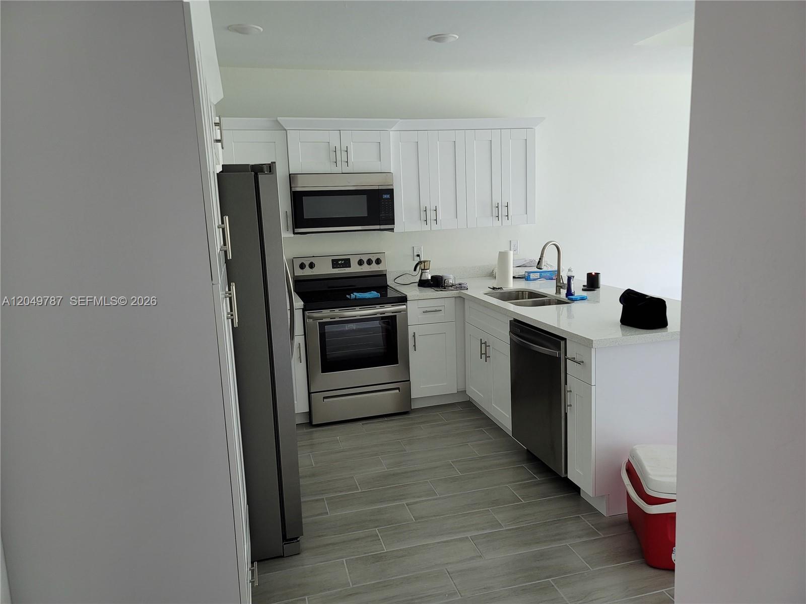 A kitchen features white cabinets, stainless steel appliances, quartz countertops, and gray tile flooring — 610 W 12, Lehigh Acres FL 33972, LEHIGH ACRES, FL