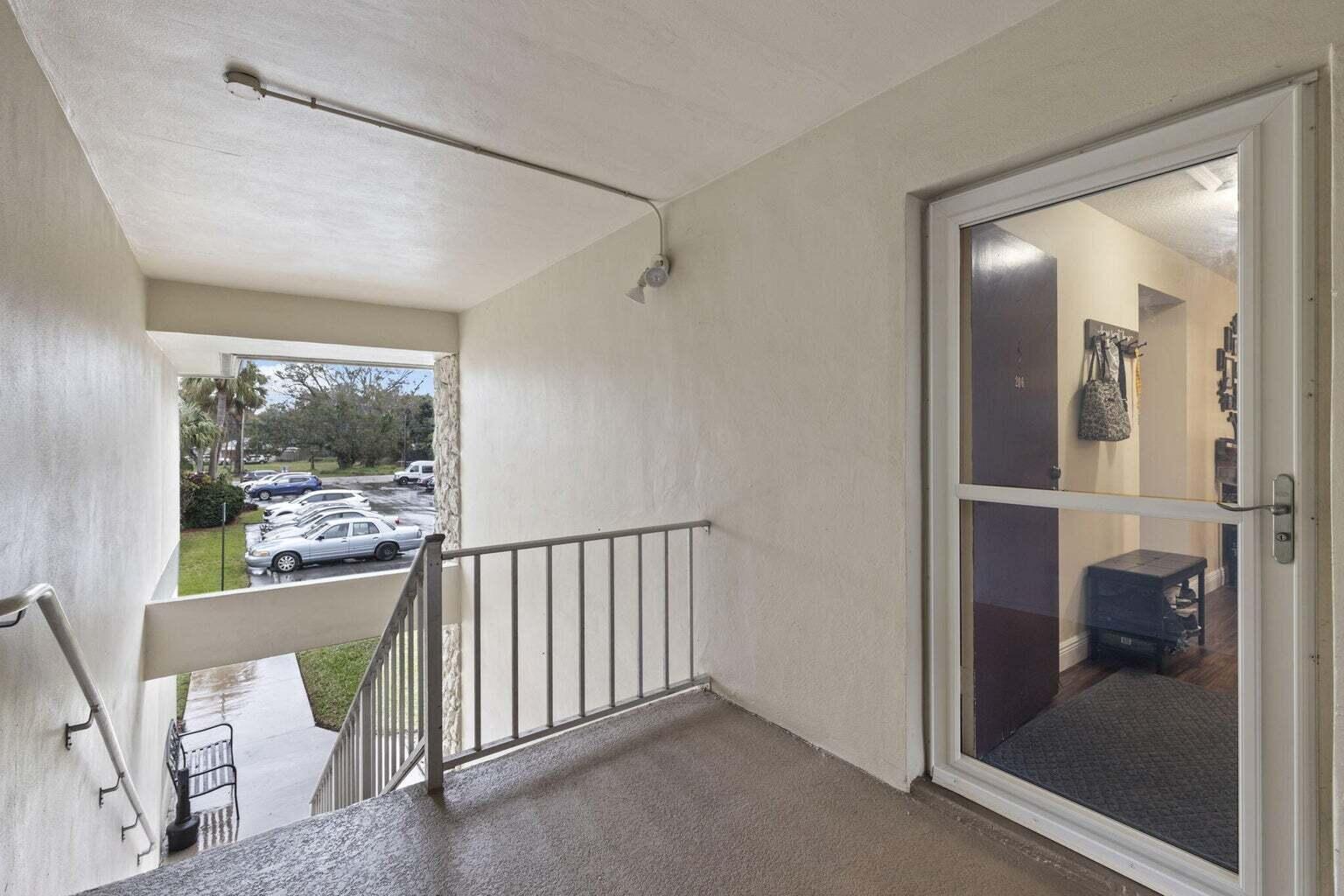 An outdoor apartment balcony with a metal railing overlooks a parking lot and stairs — 2302 Sunrise Boulevard # 206, Fort Pierce FL 34982, FORT PIERCE, FL