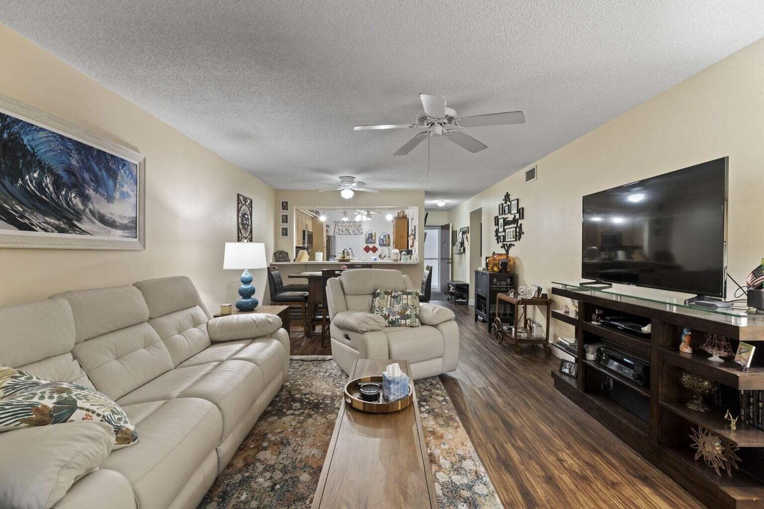 A living room features a light-colored sofa, a recliner, a television console, and wood flooring — 2302 Sunrise Boulevard # 206, Fort Pierce FL 34982, FORT PIERCE, FL