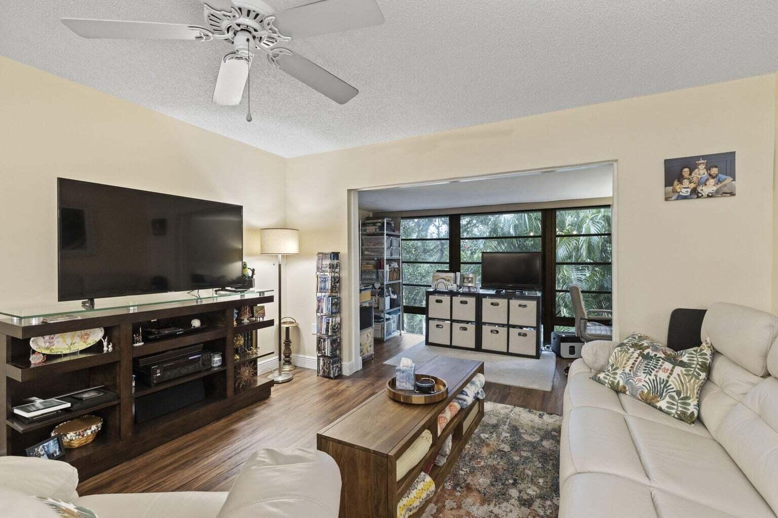 A living room with a ceiling fan, wood-look flooring, and an adjacent sunroom area — 2302 Sunrise Boulevard # 206, Fort Pierce FL 34982, FORT PIERCE, FL