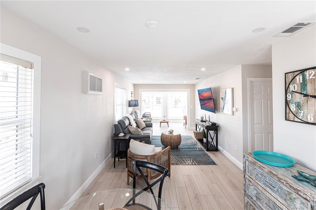 A living room features light wood flooring, a gray sofa, and a large wall clock — 6020 MIDNIGHT PASS ROAD UNIT 56, SARASOTA, FL