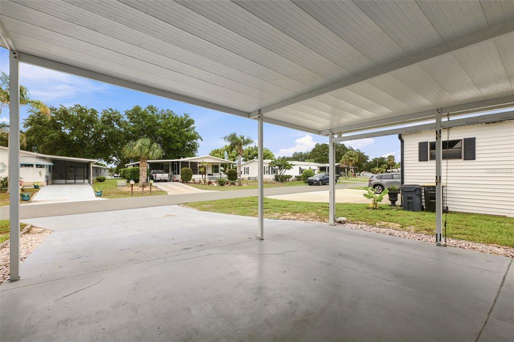 A concrete carport with a metal roof overlooks a residential street with neighboring mobile homes — 530 TIVOLI PARK DRIVE, DAVENPORT, FL