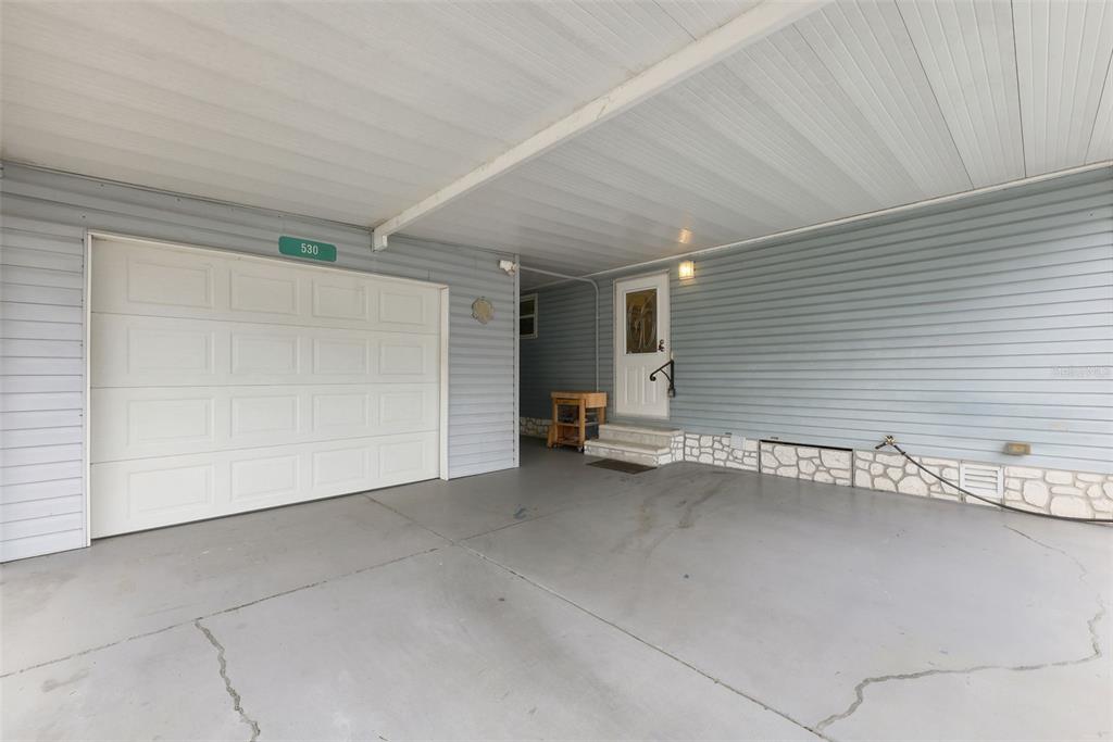A covered carport features a white garage door, light blue siding, and a stone-accented foundation — 530 TIVOLI PARK DRIVE, DAVENPORT, FL