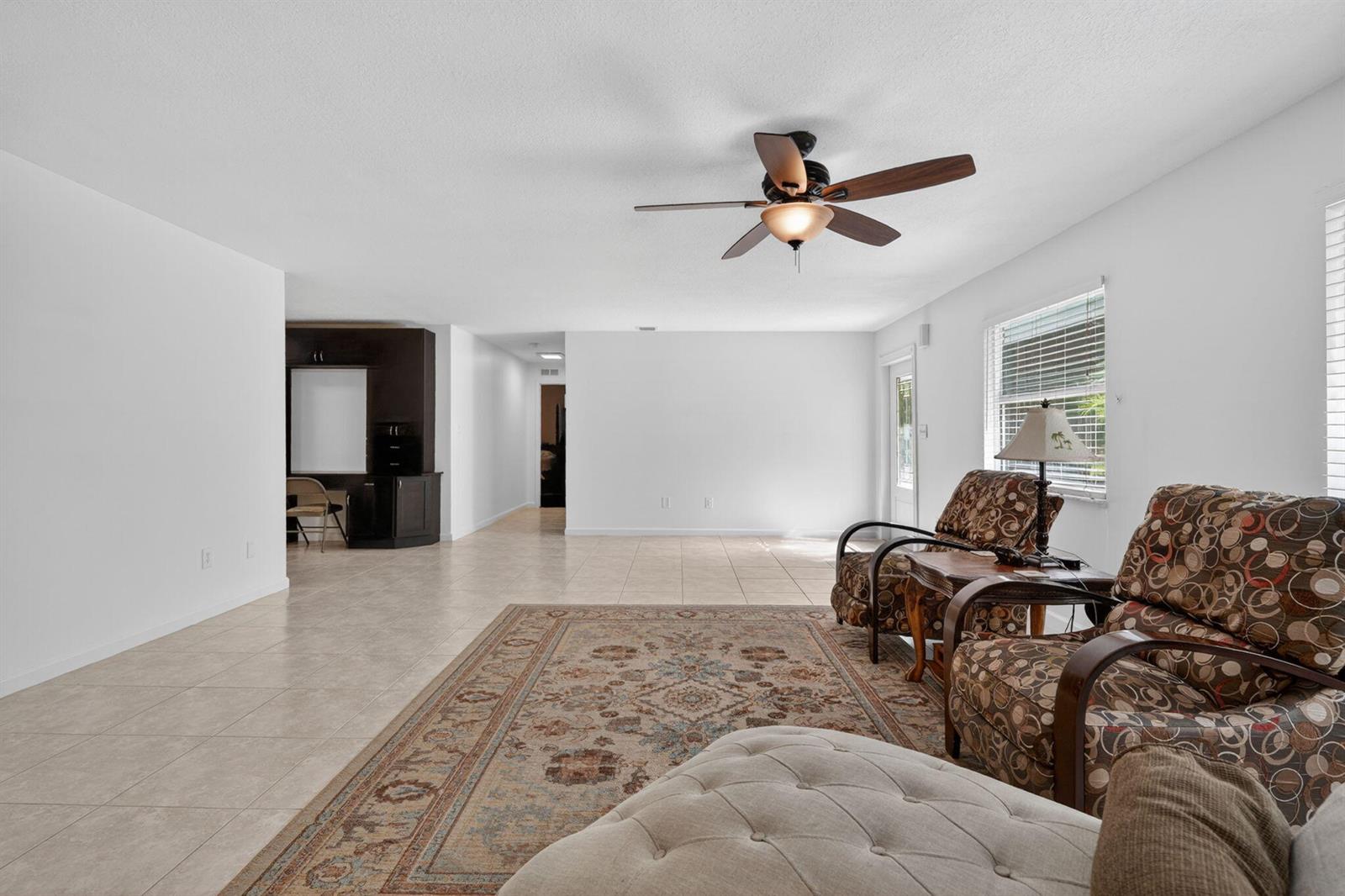 A living room features tile flooring, a ceiling fan, and two patterned armchairs on a rug — 17391 Alexander Run, Jupiter FL 33478, JUPITER, FL