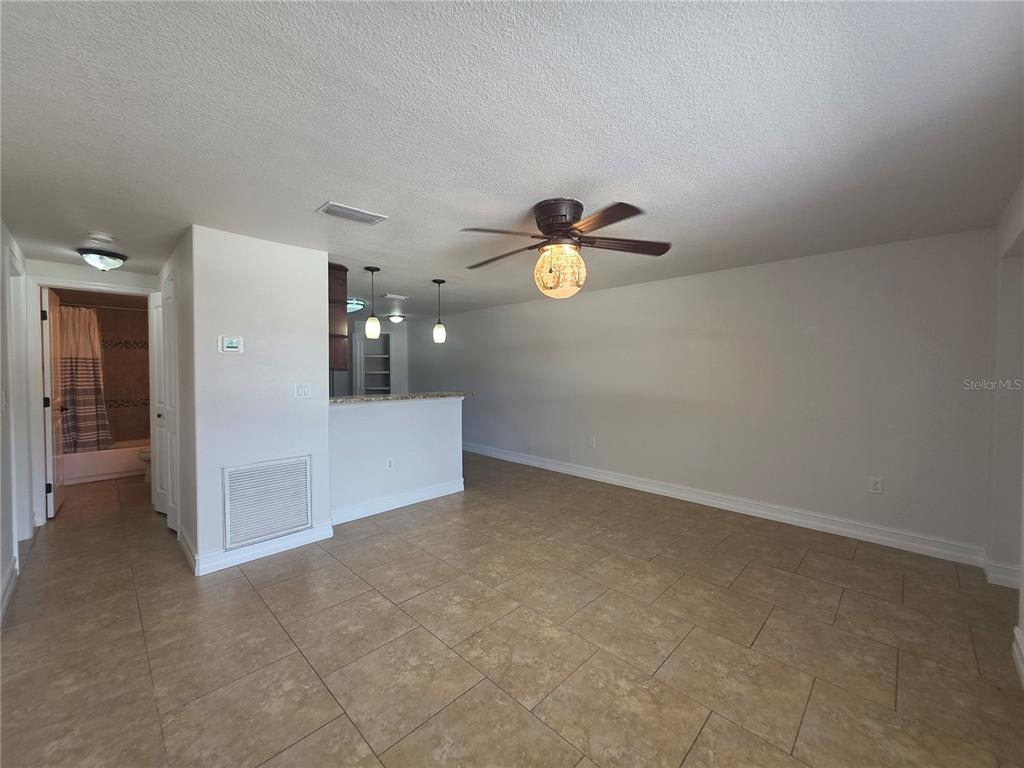 A tiled living area features a ceiling fan, a breakfast bar, and an adjacent bathroom — 15532 CHAMBERLAIN BOULEVARD UNIT A, PORT CHARLOTTE, FL