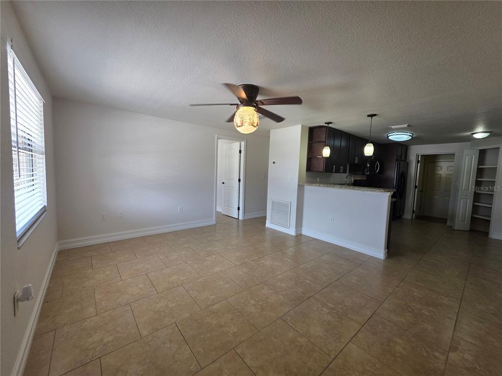An open-concept living area features tile flooring, a ceiling fan, and an adjacent kitchen — 15532 CHAMBERLAIN BOULEVARD UNIT A, PORT CHARLOTTE, FL