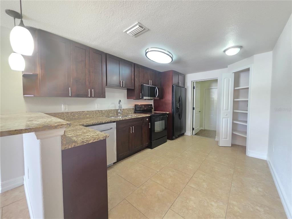 A kitchen features dark wood cabinets, granite countertops, black appliances, and light-colored tile flooring — 15532 CHAMBERLAIN BOULEVARD UNIT A, PORT CHARLOTTE, FL
