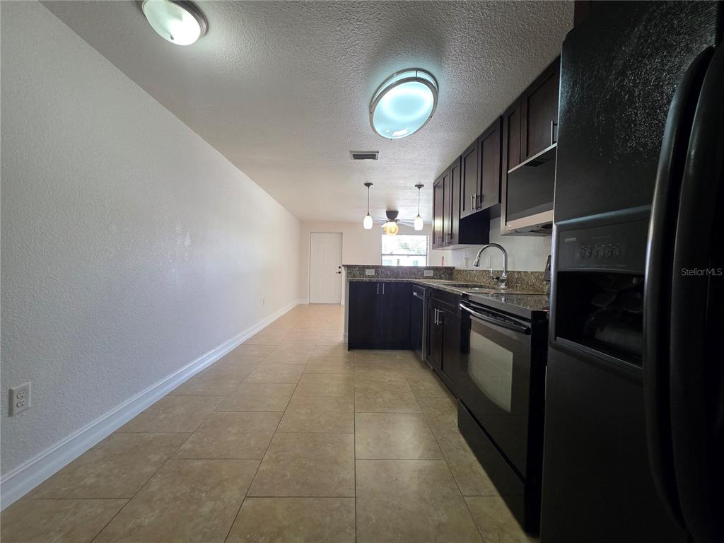 A kitchen features dark cabinetry, granite countertops, stainless steel appliances, and light-colored tile flooring — 15532 CHAMBERLAIN BOULEVARD UNIT A, PORT CHARLOTTE, FL