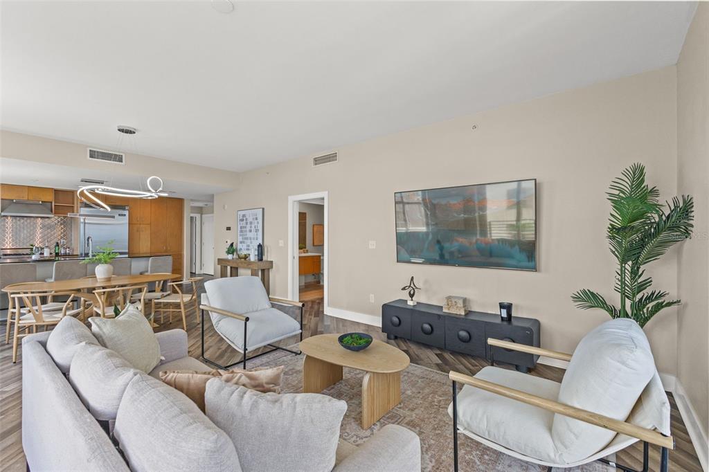 A living room with wood-look flooring, a grey sofa, and an open kitchen beyond — 1120 E KENNEDY BOULEVARD UNIT 1229, TAMPA, FL