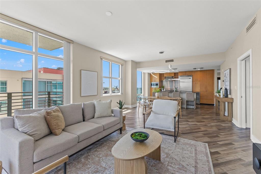 A living room and kitchen area with light wood flooring, neutral furniture, and large windows — 1120 E KENNEDY BOULEVARD UNIT 1229, TAMPA, FL