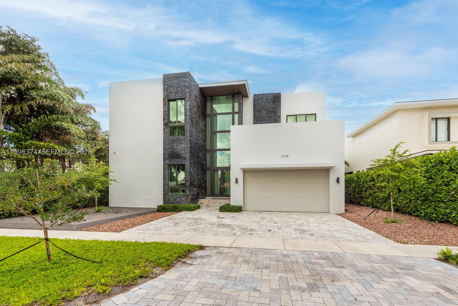 A modern two-story house features a stone facade, large glass windows, and a paved driveway — 13145 Coronado Ln, North Miami FL 33181, NORTH MIAMI, FL