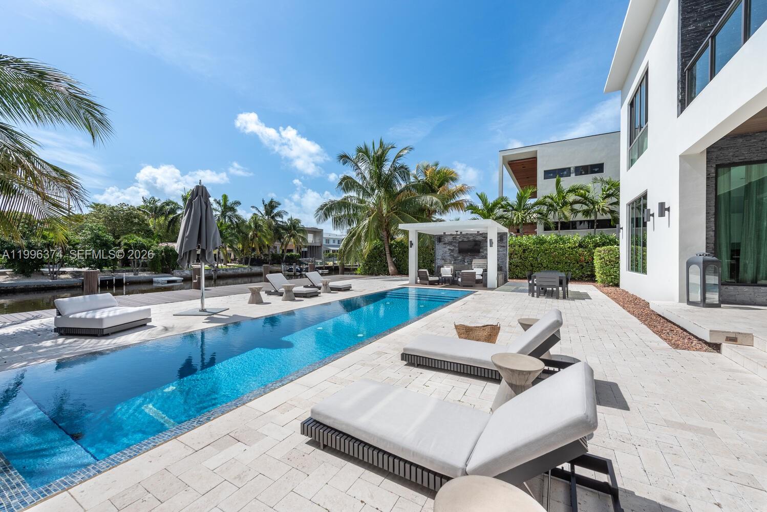 A modern backyard features a rectangular swimming pool, lounge chairs, and a covered patio area — 13145 Coronado Ln, North Miami FL 33181, NORTH MIAMI, FL