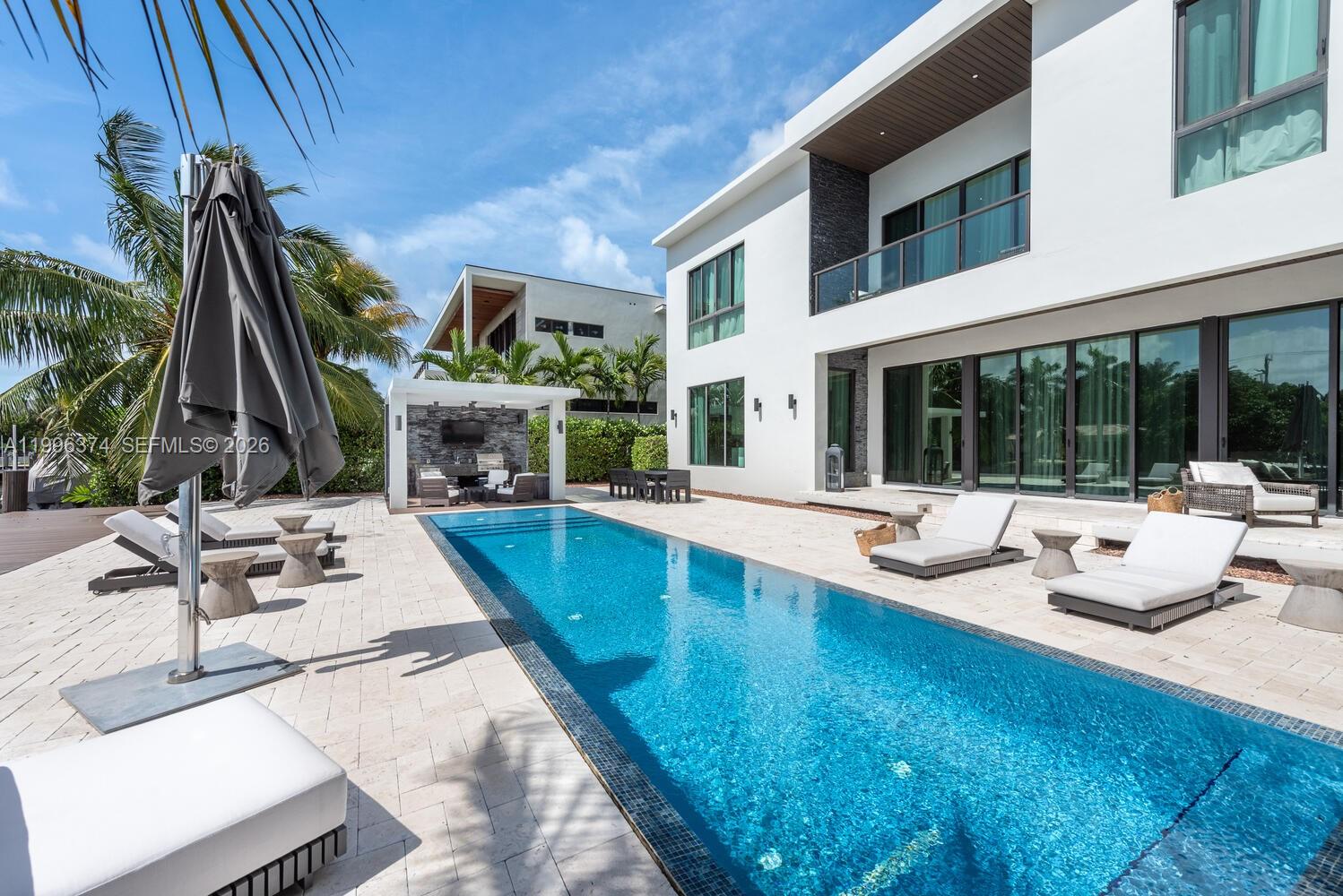 A modern two-story house features a rectangular swimming pool and a covered outdoor lounge area — 13145 Coronado Ln, North Miami FL 33181, NORTH MIAMI, FL
