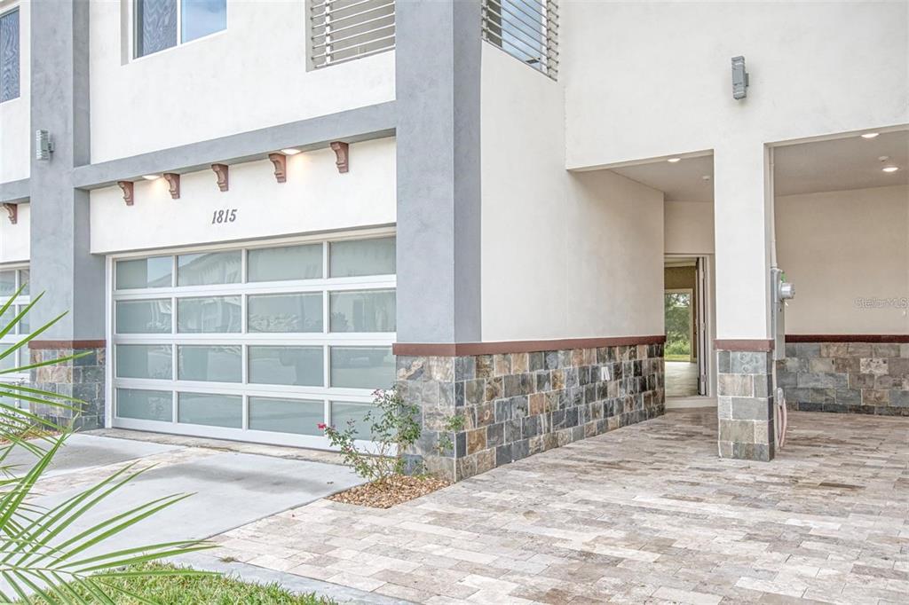 A modern home exterior features a glass-paneled garage door, stone veneer siding, and a paved driveway — 1815 BRENTWOOD COURT, DAVENPORT, FL