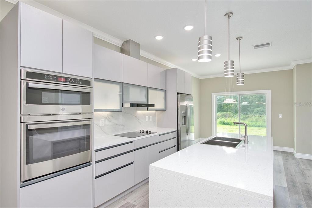 A modern kitchen features white cabinetry, stainless steel appliances, a quartz island, and sliding doors — 1815 BRENTWOOD COURT, DAVENPORT, FL