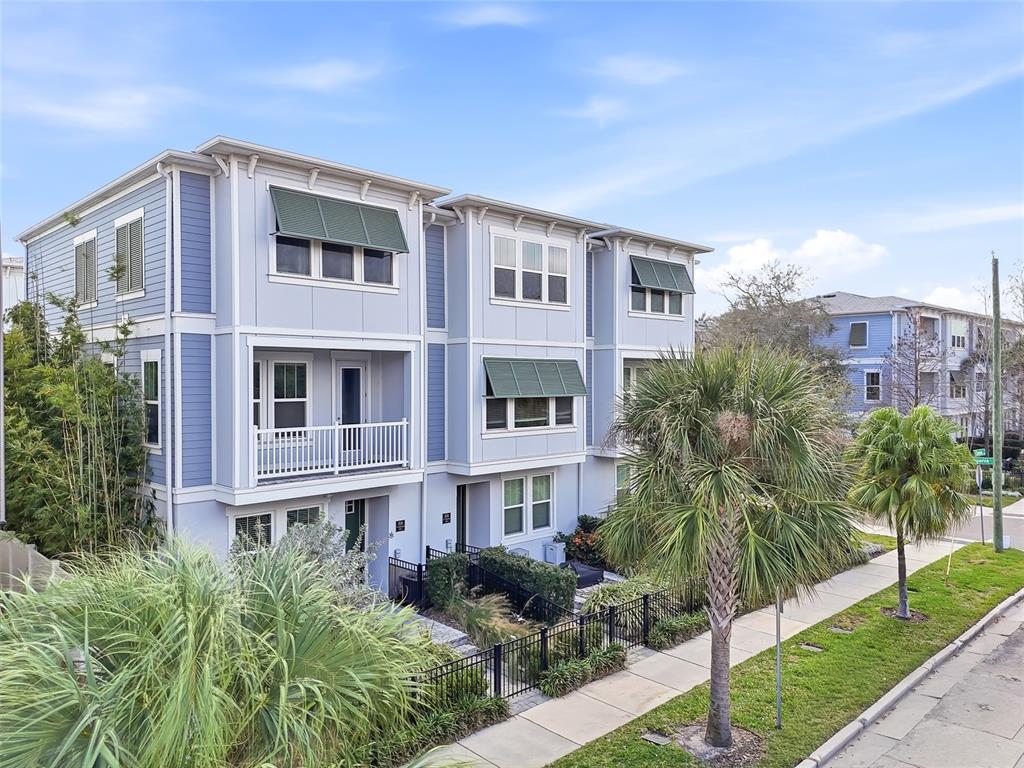 A three-story light blue townhouse with green awnings and a balcony stands near a sidewalk — 2510 W CLEVELAND STREET UNIT 2, TAMPA, FL
