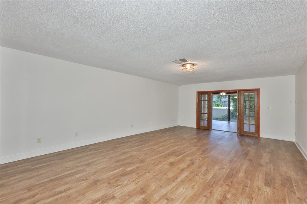 A spacious room with light wood-look flooring, white walls, and French doors leading outside — 2823 HERON PLACE, CLEARWATER, FL