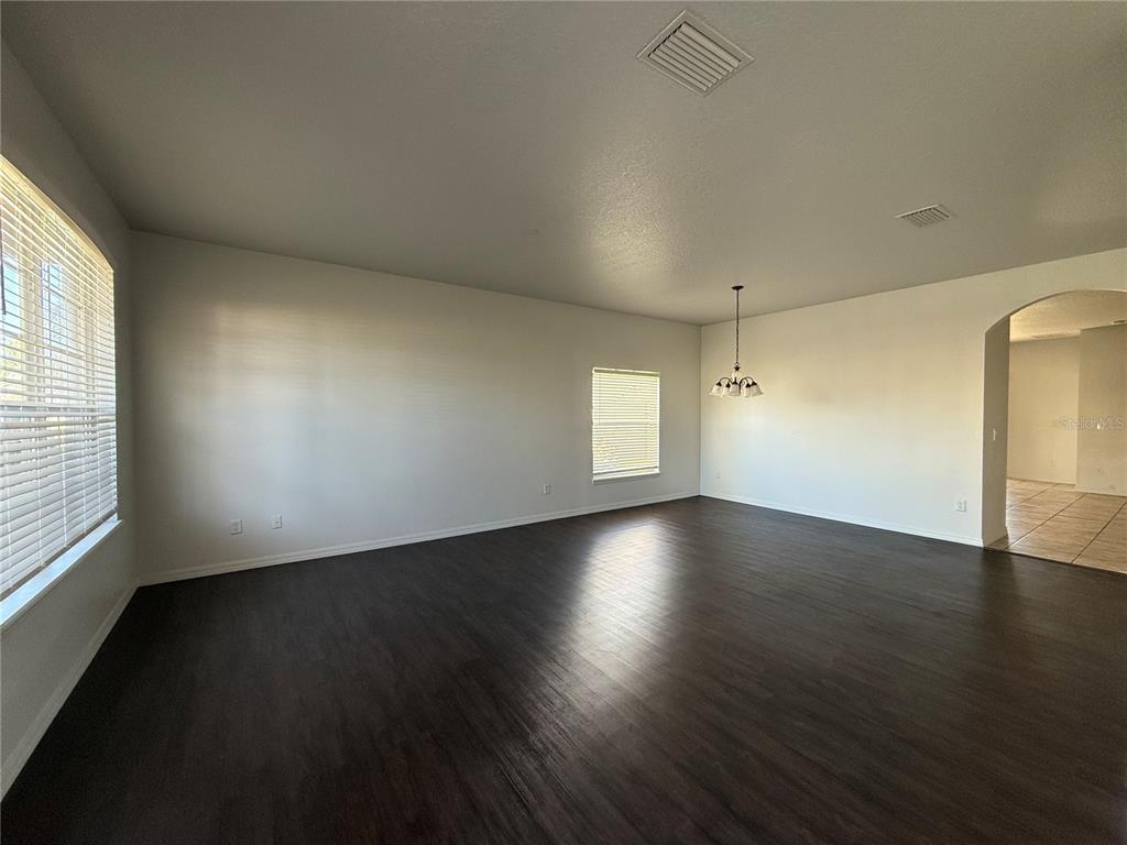 An empty room features dark wood-look flooring, white walls, two windows, and a hanging light fixture — 368 CONCH KEY WAY, SANFORD, FL