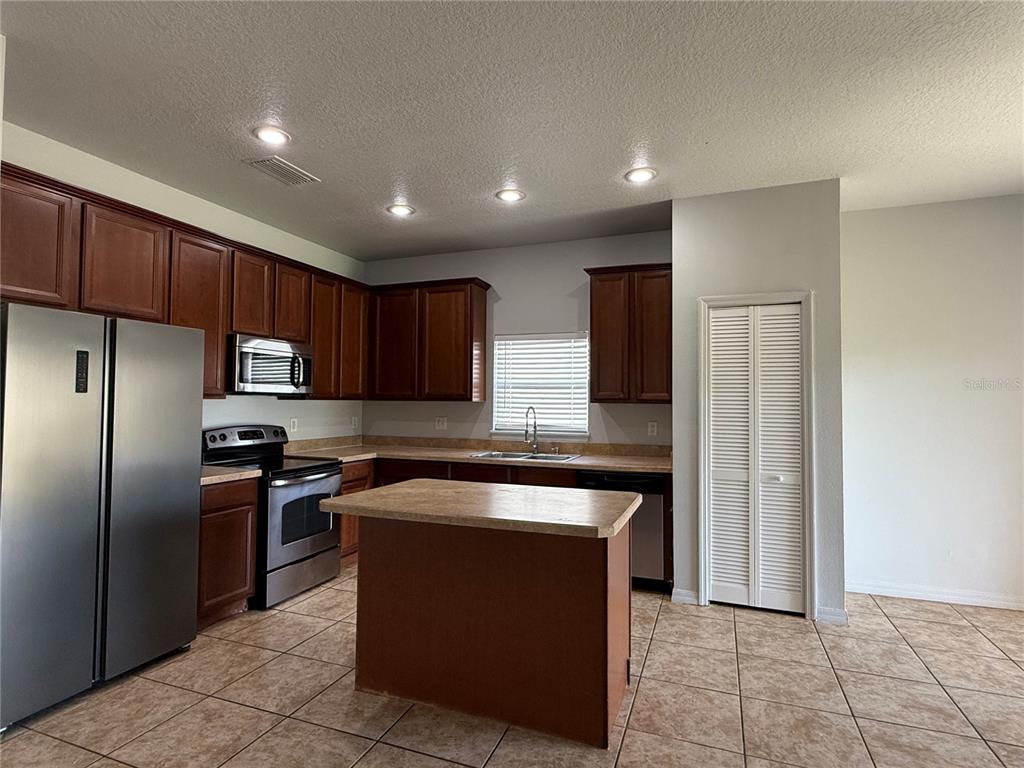 A kitchen features dark wood cabinets, stainless steel appliances, a center island, and tile flooring — 368 CONCH KEY WAY, SANFORD, FL
