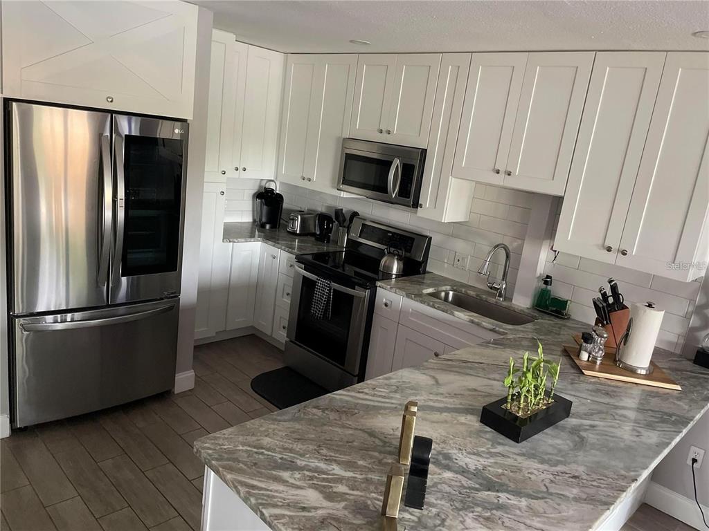 A kitchen features white cabinets, stainless steel appliances, and a gray marble-patterned countertop — 2595 CYPRUS DRIVE UNIT 4-217, PALM HARBOR, FL