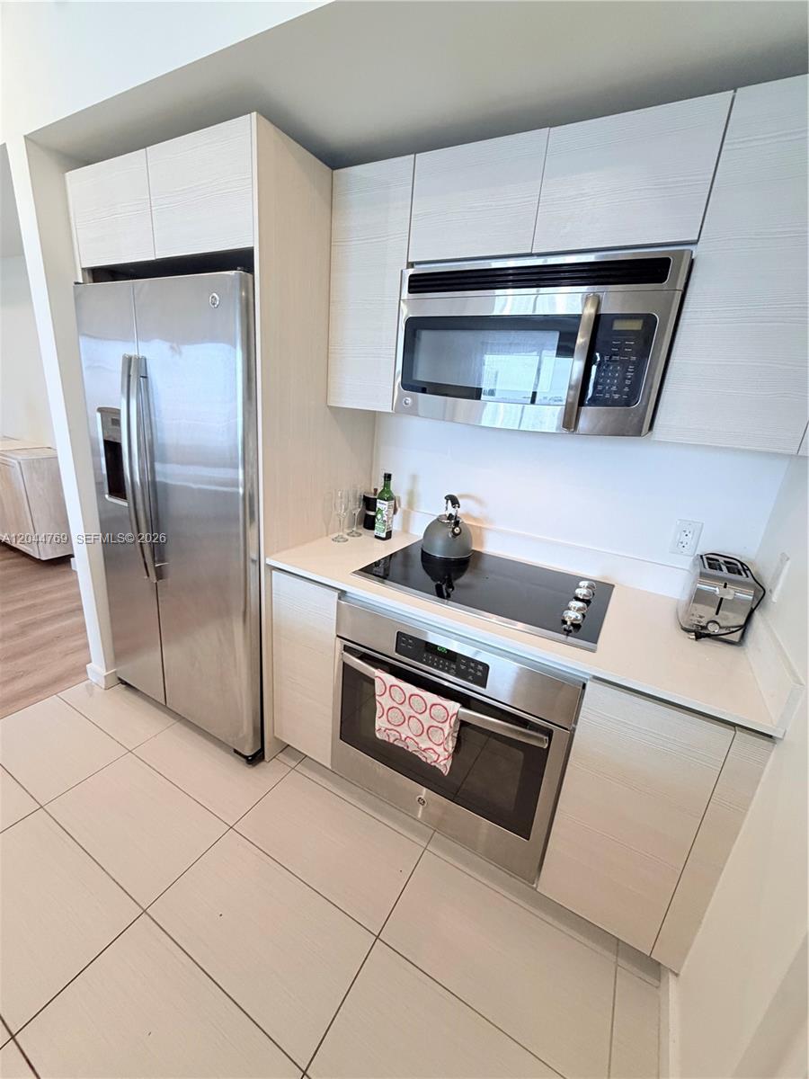 A modern kitchen features light wood-grain cabinets, stainless steel appliances, and white tile flooring — 4250 Biscayne Blvd # 1617, Miami FL 33137, MIAMI, FL