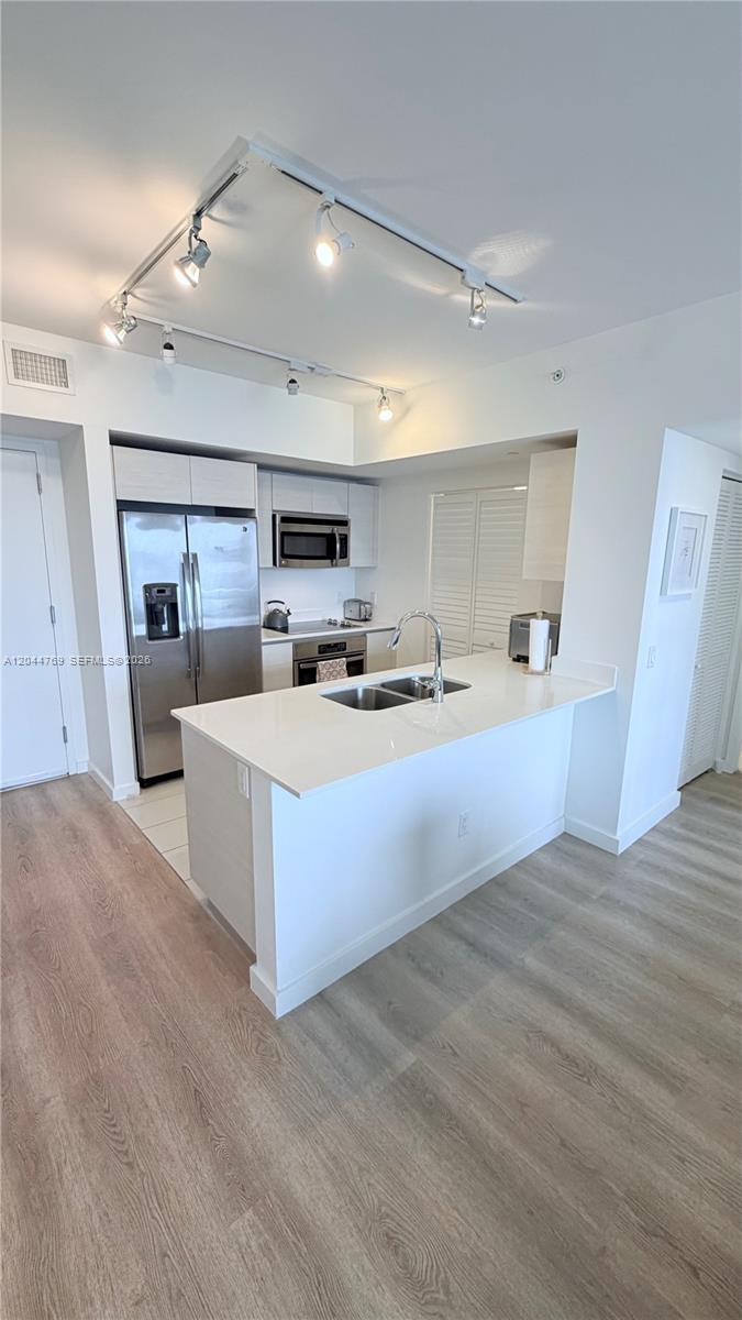 A modern kitchen features white cabinetry, stainless steel appliances, a quartz island, and track lighting — 4250 Biscayne Blvd # 1617, Miami FL 33137, MIAMI, FL