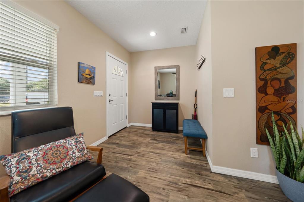 An entryway features wood-look flooring, a white front door, a mirror, and a blue bench — 401 DEMPSEY ROAD, PALM HARBOR, FL