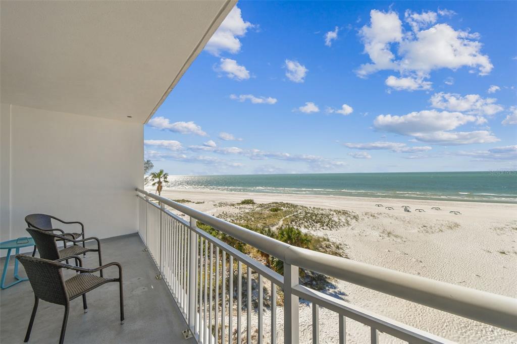A balcony with chairs overlooks a sandy beach and the ocean under a blue sky — 10116 GULF BOULEVARD UNIT 502W, TREASURE ISLAND, FL