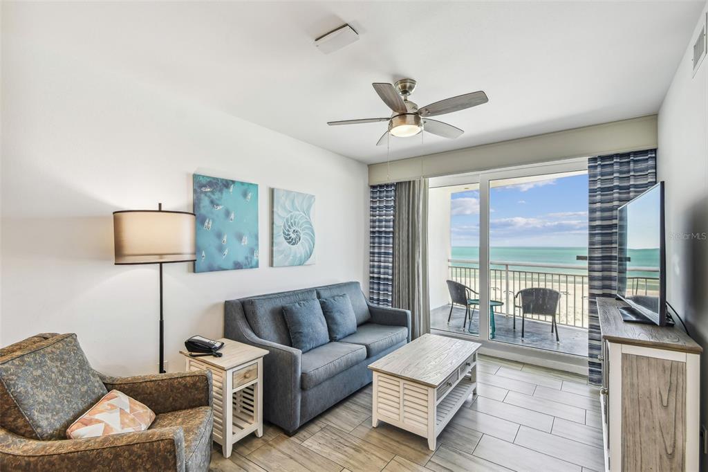 A living room features a sofa, armchair, coffee table, and a balcony overlooking the ocean — 10116 GULF BOULEVARD UNIT 502W, TREASURE ISLAND, FL