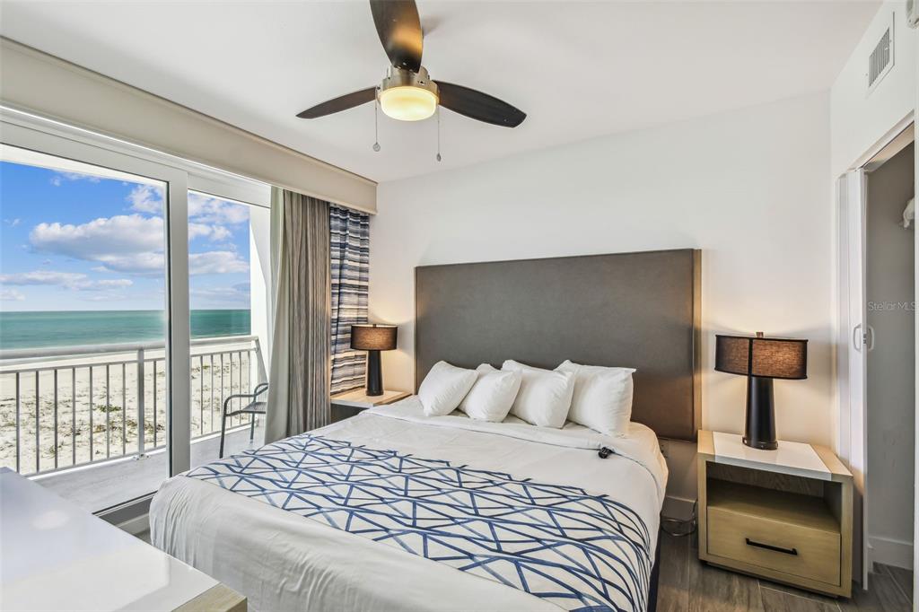 A bedroom features a bed, two lamps, a ceiling fan, and a balcony overlooking the ocean — 10116 GULF BOULEVARD UNIT 502W, TREASURE ISLAND, FL