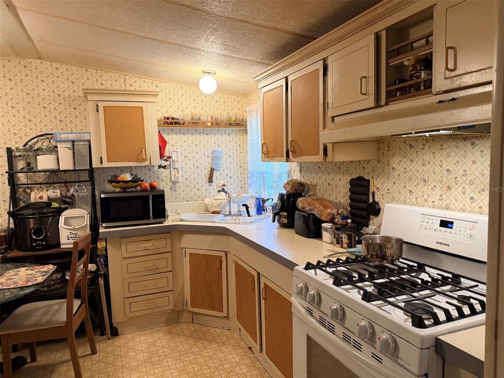A kitchen features light-colored cabinets, patterned wallpaper, a gas stove, and a corner sink — 355 NE 436 AVENUE, OLD TOWN, FL