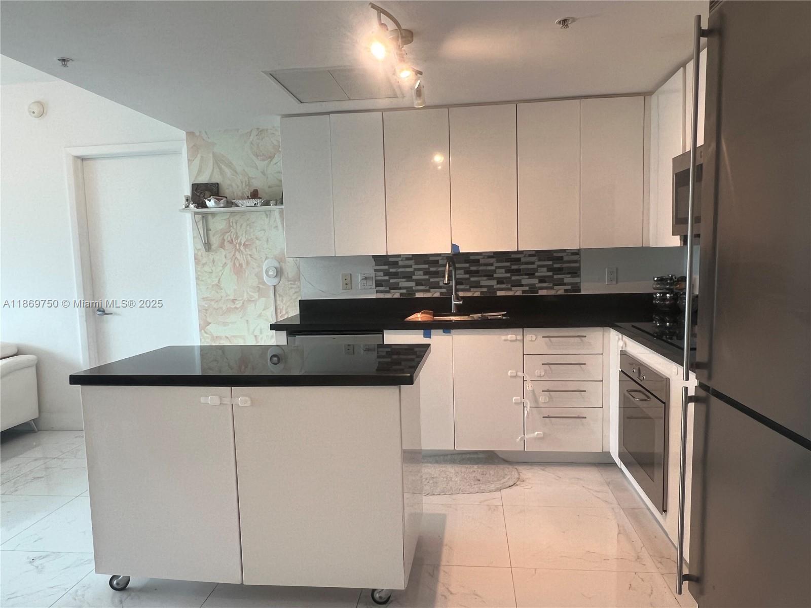 A kitchen features white cabinets, a black countertop, a rolling island, and a floral accent wall — 92 SW 3rd St # 3803, Miami FL 33130, MIAMI, FL