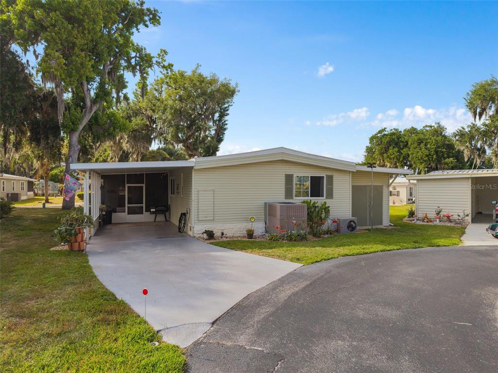 A light-colored mobile home features a concrete driveway, a carport, and a small storage shed — 4 GALLINULE COURT, FRUITLAND PARK, FL