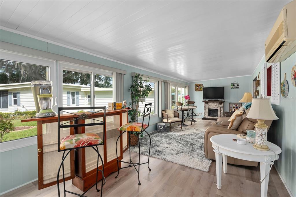 A sunroom features light blue walls, wood-look flooring, a bar area, and a seating space — 4 GALLINULE COURT, FRUITLAND PARK, FL
