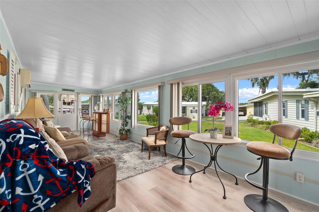 A sunroom with light wood flooring, large windows, a sofa, and a small bistro table — 4 GALLINULE COURT, FRUITLAND PARK, FL