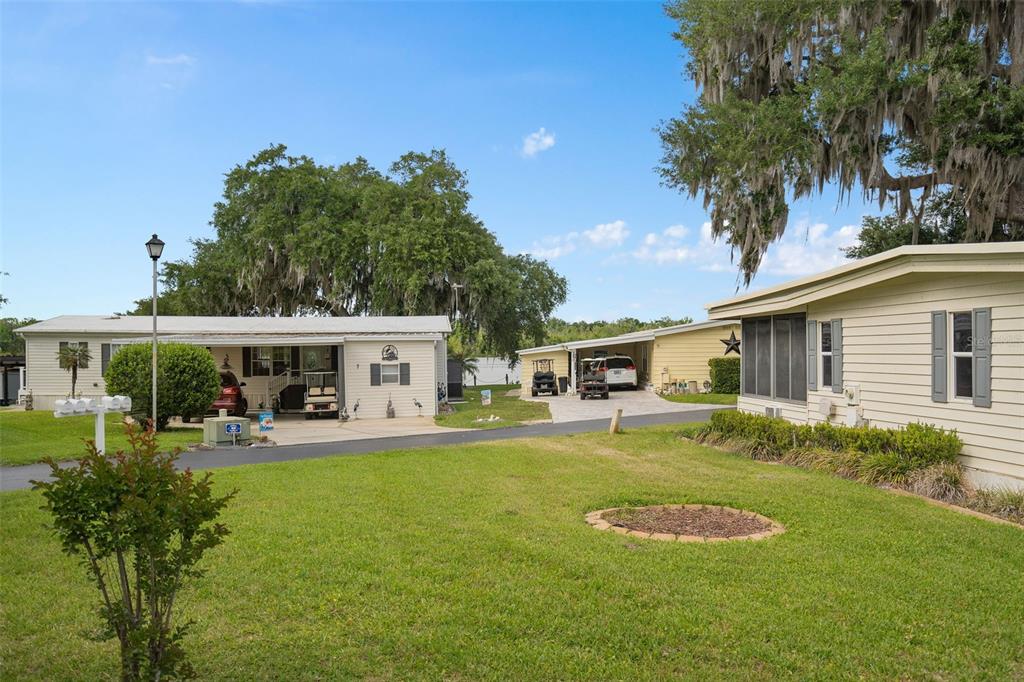 A view of two mobile homes with carports and a grassy yard under large trees — 4 GALLINULE COURT, FRUITLAND PARK, FL