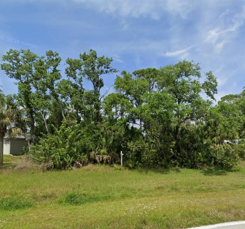 A vacant, grassy lot features a dense cluster of trees and a small white sign — 9196 WILLMINGTON BOULEVARD, ENGLEWOOD, FL