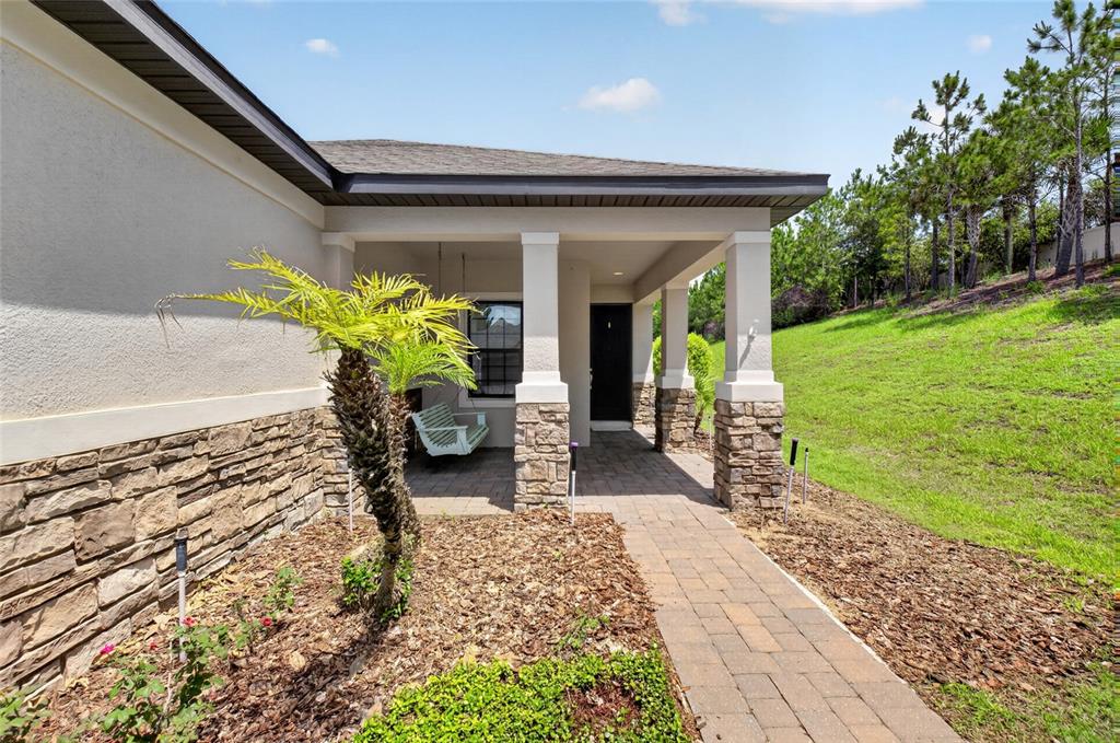 A stone-accented house exterior features a covered porch with a swing and a paved walkway — 2612 FRAZEEK COURT, CLERMONT, FL